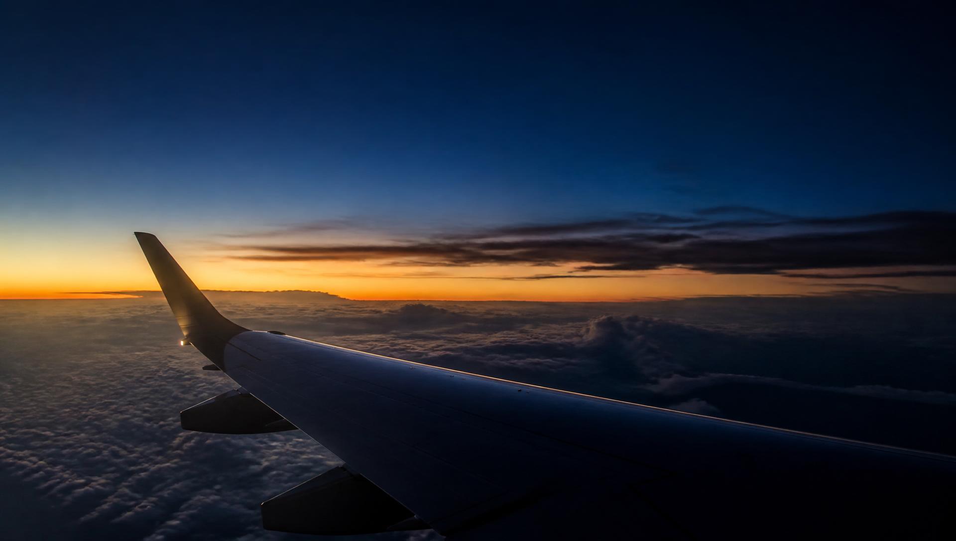 Asa de avião sobrevoando nuvens ao entardecer